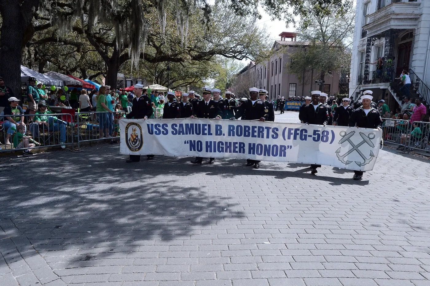 Sailors marching with a banner past crowds in green along an oak-shaded Savannah street